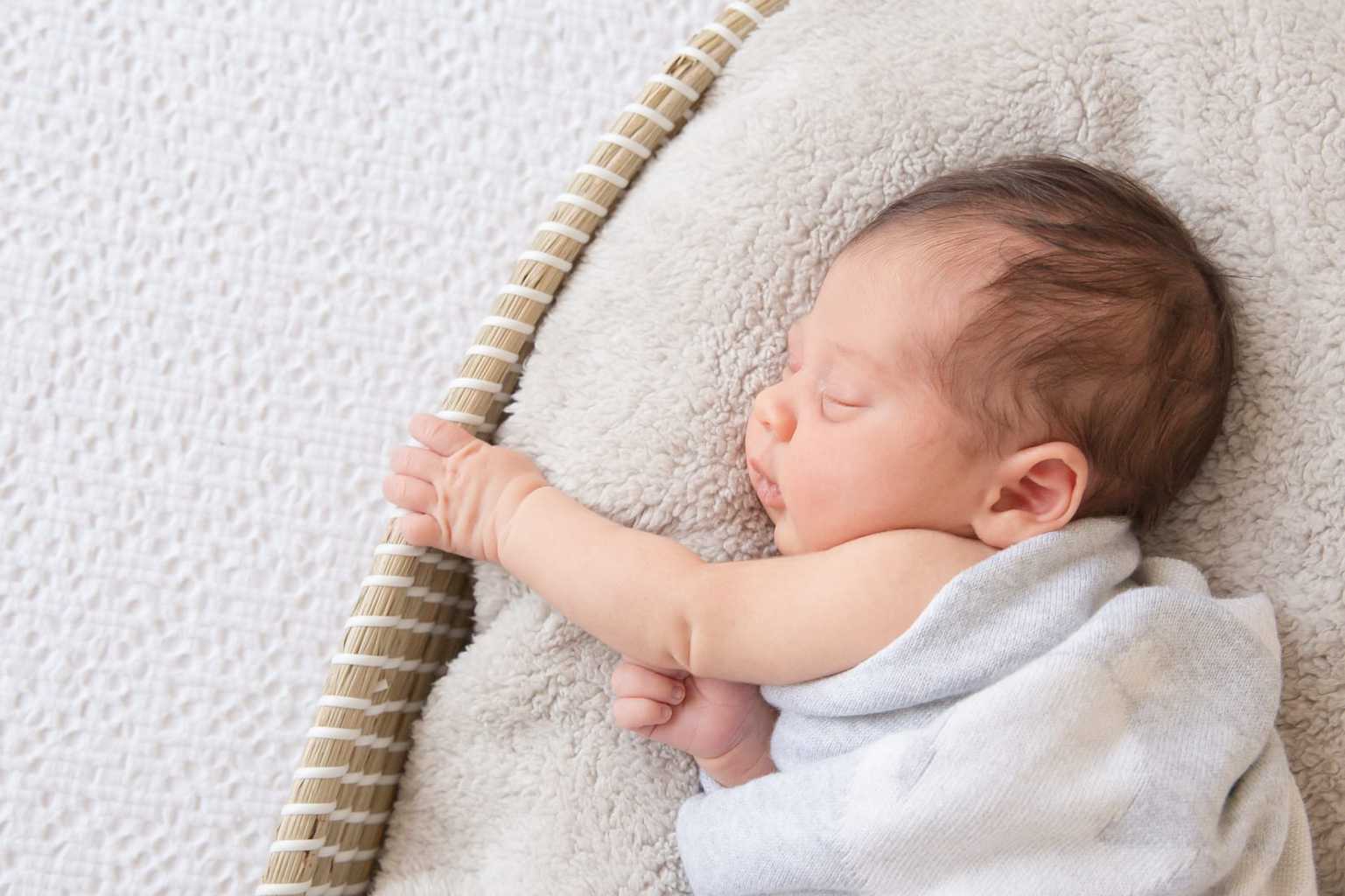 Photo of small baby sleeping in a towel on a cushion.Photo by Bright Photography.