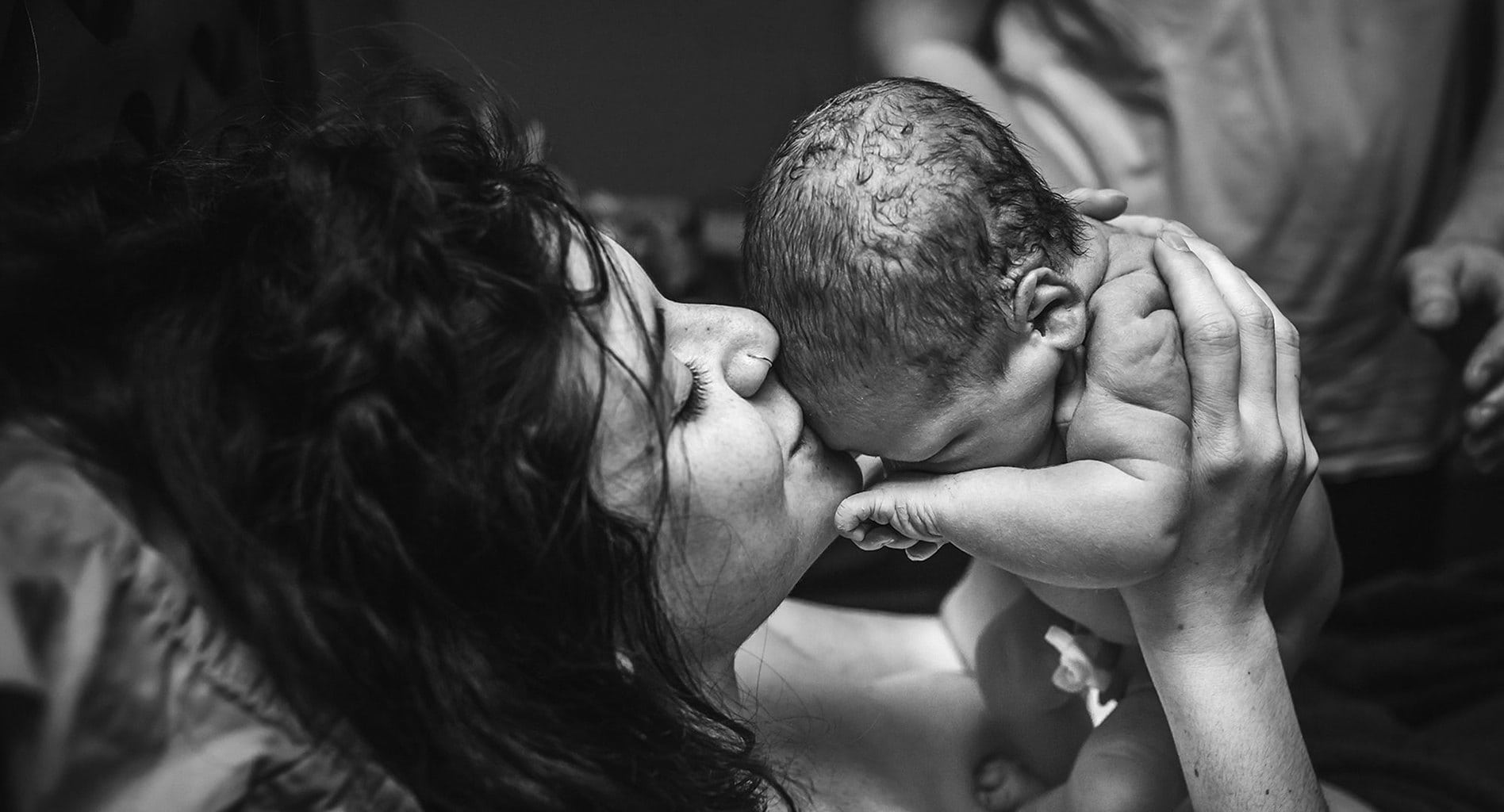 Woman kissing her newborn baby on the forehead. Photo by Monet Nicole