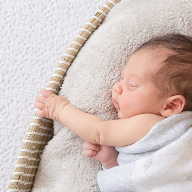 Photo of small baby sleeping in a towel on a cushion.Photo by Bright Photography.
